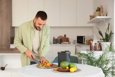 Mutfakta yemek pişirirken gübre kutusu ve sebze artıklarıyla gezen genç adam.