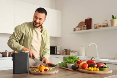 Mutfakta yemek pişirirken gübre kutusu ve sebze artıklarıyla gezen genç adam.