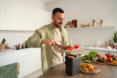 Mutfakta yemek pişirirken gübre kutusu ve sebze artıklarıyla gezen genç adam.