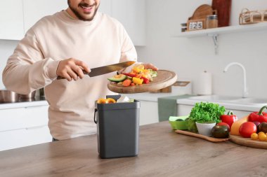 Mutfakta yemek pişirirken gübre kutusu ve sebze artıklarıyla gezen genç adam.