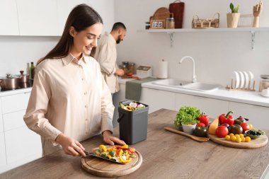 Mutfakta yemek pişirirken gübre kutusu ve sebze artıklarıyla gezen genç bir kadın.