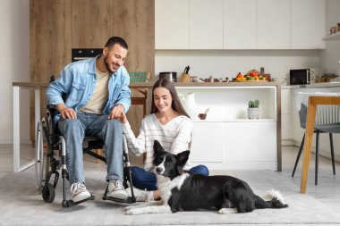 Tekerlekli sandalyedeki genç adam, karısı ve köpeği evde.