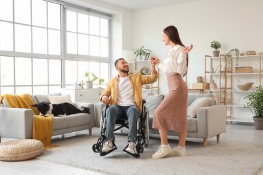 Tekerlekli sandalyedeki genç adam ve evde dans eden karısı.