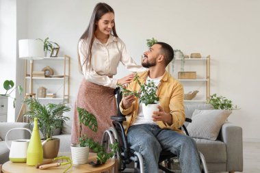 Tekerlekli sandalyedeki genç adam, evde karısı ve çiçekleri var.
