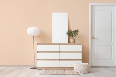 Koridordaki bej duvarın yanında klozet, lamba, puf ve boş poster.