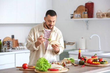 Genç adam mutfakta lezzetli Meksika tacoları hazırlıyor.