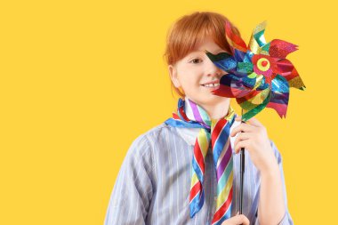 Sarı arka planda yel değirmeni oyuncağı olan mutlu kızıl kız.