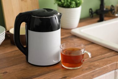 Modern elektrikli su ısıtıcısı ve bir bardak sıcak çay mutfakta tezgahta.