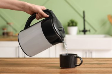 Kadın modern elektrikli çaydanlıktan su dolduruyor mutfaktaki ahşap masaya.