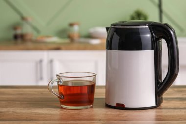 Modern elektrikli su ısıtıcısı ve bir bardak sıcak çay mutfaktaki ahşap masada.