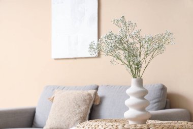 Oturma odasındaki rahat kanepenin yanındaki sehpanın üzerinde çingene çiçekleri olan vazo.