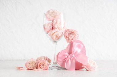 Gül çiçekli kompozisyon, hediye kutusu ve beyaz grunge arka planda şarap kadehi. Sevgililer Günü kutlaması