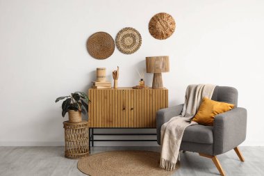 Oturma odasının içinde, beyaz duvarın yanında koltuk ve çekmeceler var.