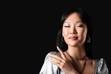 Siyah arka planda gümüş bluzlu düşünceli Asyalı kadın.