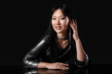 Siyah arka planda gümüş bluzlu genç Asyalı kadın.