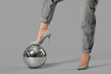 Topuklu ayakkabılı genç bir kadın ve gri arka planda disko topu.