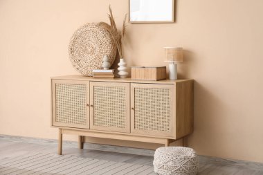 Oturma odasının içi. Bej duvarın yanında çekmeceler var.