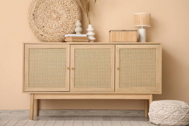 Oturma odasının içi. Bej duvarın yanında çekmeceler var.