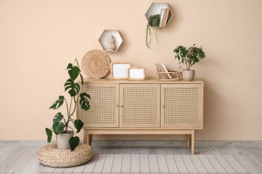 Oturma odasının içinde çekmeceler ve bej duvarın yanında bitkiler var.