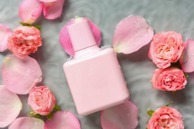 Bir şişe parfüm, güzel pembe güller ve gri arka planda suda yapraklar.