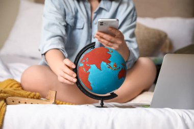 Yatak odasında cep telefonu kullanan, dünyayı gezen bir kadın, yakın plan. Güzergah kavramı
