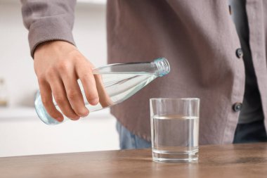 Evinde bardağa su döken genç adam, yakın plan.