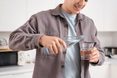 Evinde bardağa su döken genç adam, yakın plan.