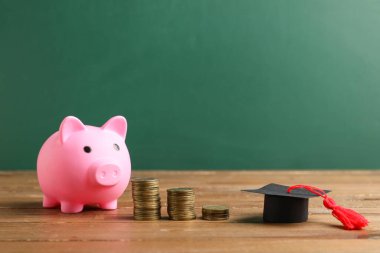 Mezuniyet şapkası ve bozuk paralarla yeşil tahtanın yanındaki masada kumbarada. Öğrenci kredisi kavramı