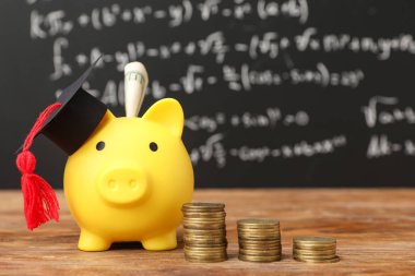 Mezuniyet şapkası ve kara tahtanın yanındaki masada bozuk paralarla kumbarada. Öğrenci kredisi kavramı