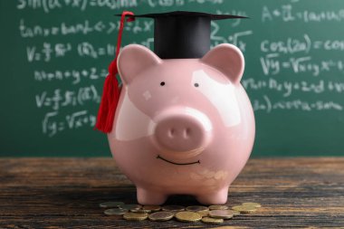 Mezuniyet şapkası ve bozuk paralarla yeşil tahtanın yanındaki masada kumbarada. Öğrenci kredisi kavramı