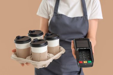 Bej arka planda kağıt bardak kahve ve ödeme terminali olan bayan barista, yakın plan.