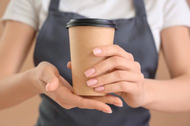 Bej arka planda bir fincan kahve ile bayan barista, yakın plan.