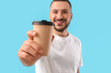 Mavi arka planda bir fincan kağıt kahve olan genç adam.
