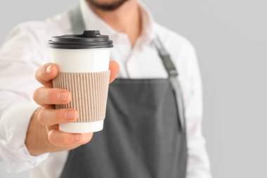Gri arka planda bir fincan kahve ile genç erkek barista, yakın plan.