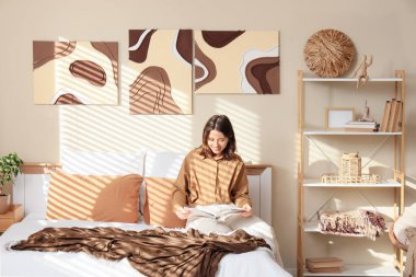 Yatak odasında yatakta dergi okuyan genç bir kadın.