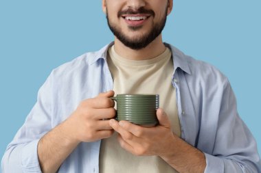 Mavi arka planda yeşil seramik bardaklı genç adam, yakın plan.