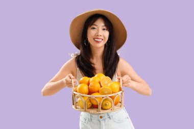 Leylak arka planında taze portakal sepeti olan genç Asyalı kadın.