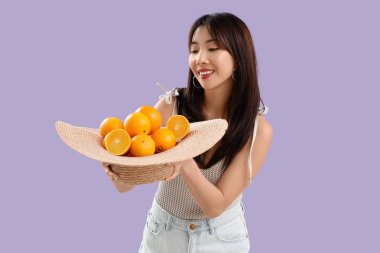 Leylak arkaplanda taze portakallarla dolu şapkası olan genç Asyalı kadın.
