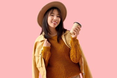 Pembe arka planda bir fincan kahvesi olan genç Asyalı kadın.