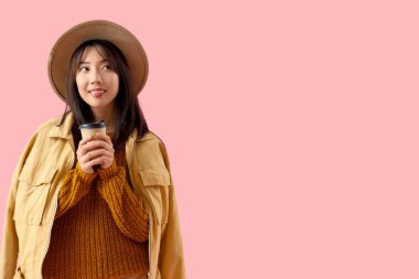 Pembe arka planda bir fincan kahvesi olan genç Asyalı kadın.