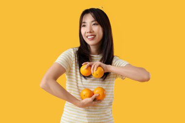 Sarı arka planda taze portakallı genç Asyalı kadın.