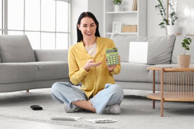 Hesap makinesi ve para iadesi formu olan genç bir kadın evde oturuyor.