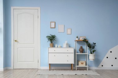 Beyaz kapısı, çekmeceleri ve mavi duvarın yanındaki raf ünitesi olan modern salonun içi.