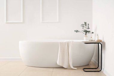 Banyonun içindeki beyaz duvarın yanındaki küvet ve masa.