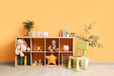 Çocuk odasının içinde raflama ünitesi ve turuncu duvarın yanındaki sandalye.