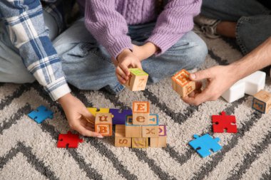 Mutlu çift ve evlatlık kız evdeki halının üstünde küplerle oynuyorlar.