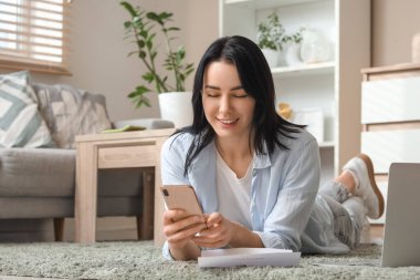 İade formuna sahip genç bir kadın evde cep telefonu kullanıyor.