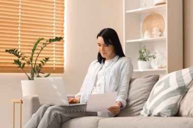 Evdeki kanepede dizüstü bilgisayar kullanan geri ödeme formu olan genç bir kadın.