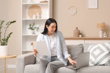 Evdeki kanepede dizüstü bilgisayar kullanan geri ödeme formu olan genç bir kadın.