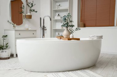 İçinde okaliptüs dalları ve küvet olan hafif bir banyo.